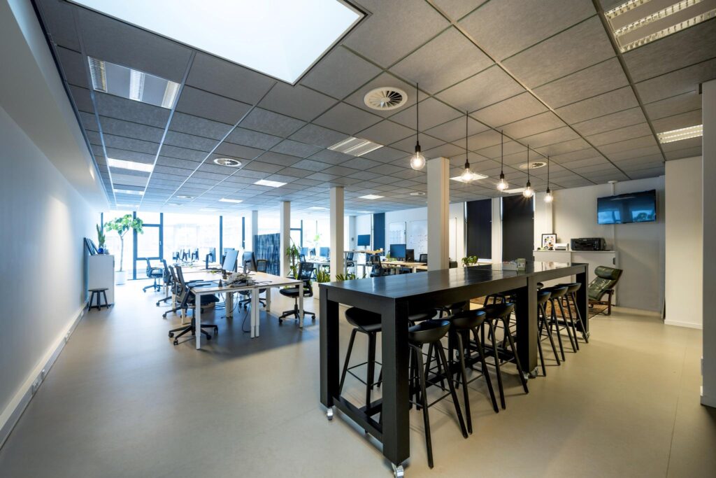 Modern ingericht kantoor aan de De Ruijterkade met flexplekken, hoge vergadertafel en grote ramen voor natuurlijk licht.